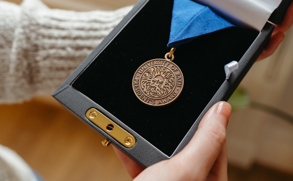 An image showing David's president's award. A gold medallion with a blue ribbon in a black box